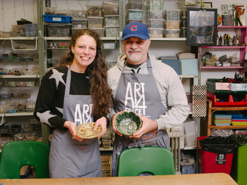 A dad and daughter smiling at a pottery class.